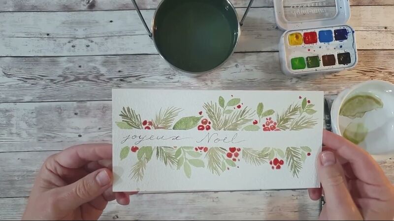 Carte de vœux horizontale : guirlande de brins de sapin et de baies rouges autour de « Joyeux Noël » écrit à l'encre.
