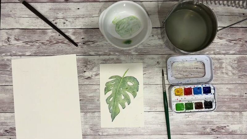 Petite aquarelle d'une feuille de Monstera en forme de cœur, aux trous laissés blancs, peinte en verts et bleus granuleux.